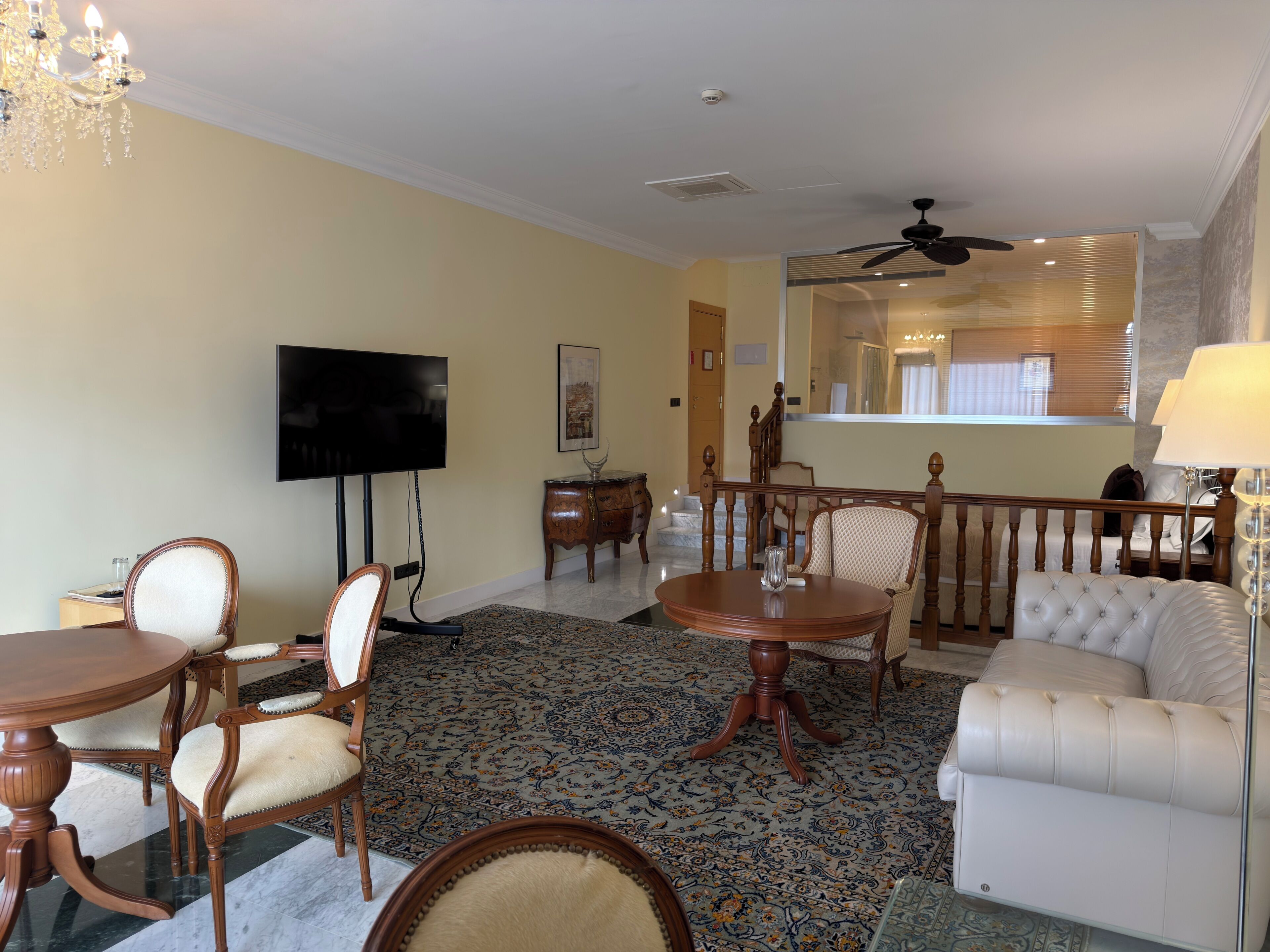 Habitación de hotel con mesa de comedor, sillas, sofá, televisor, ventilador de techo y un espejo grande.