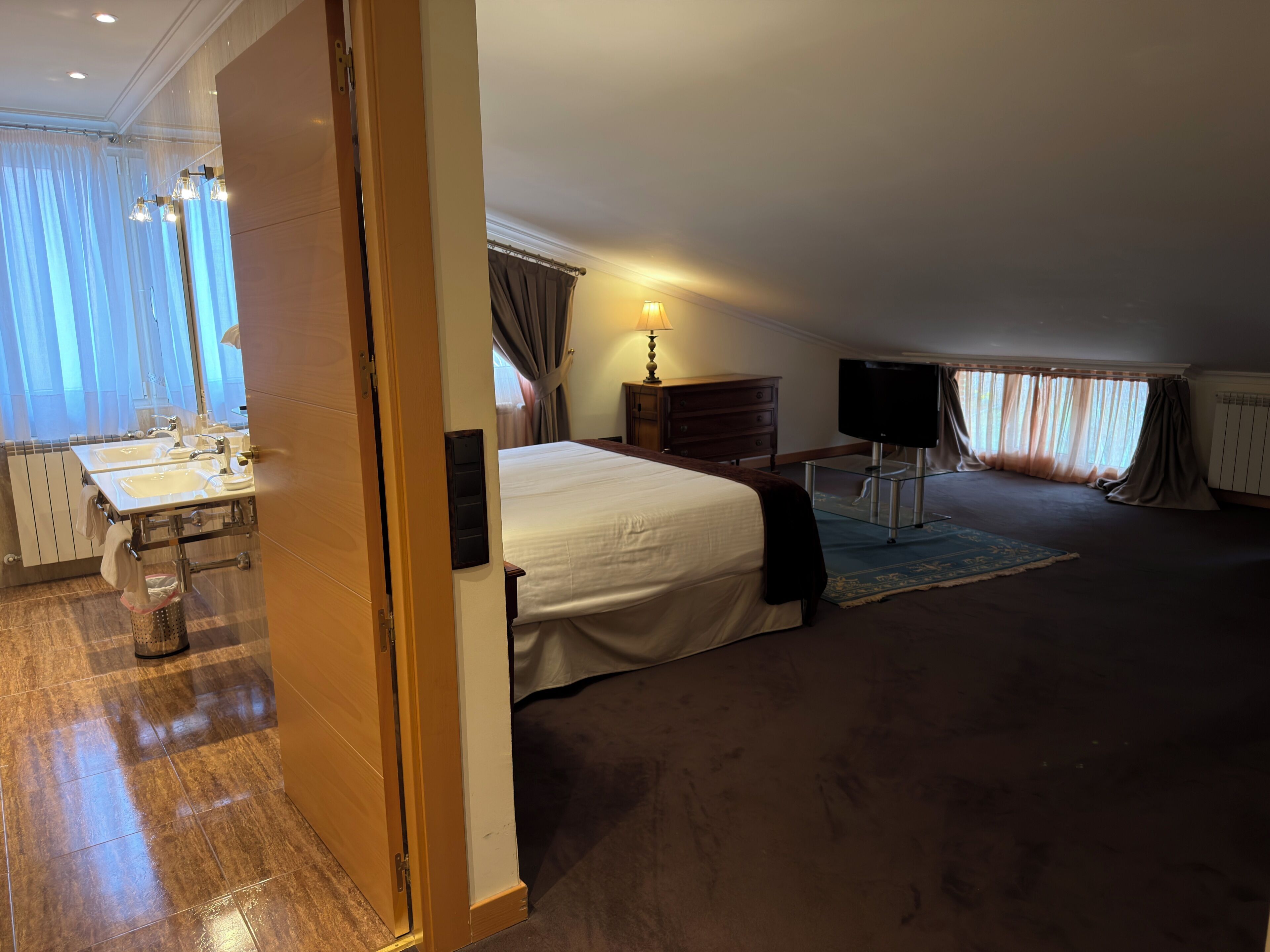 Una habitación de hotel con una cama, un escritorio con lámpara, un televisor y un baño con lavamanos y espejo.