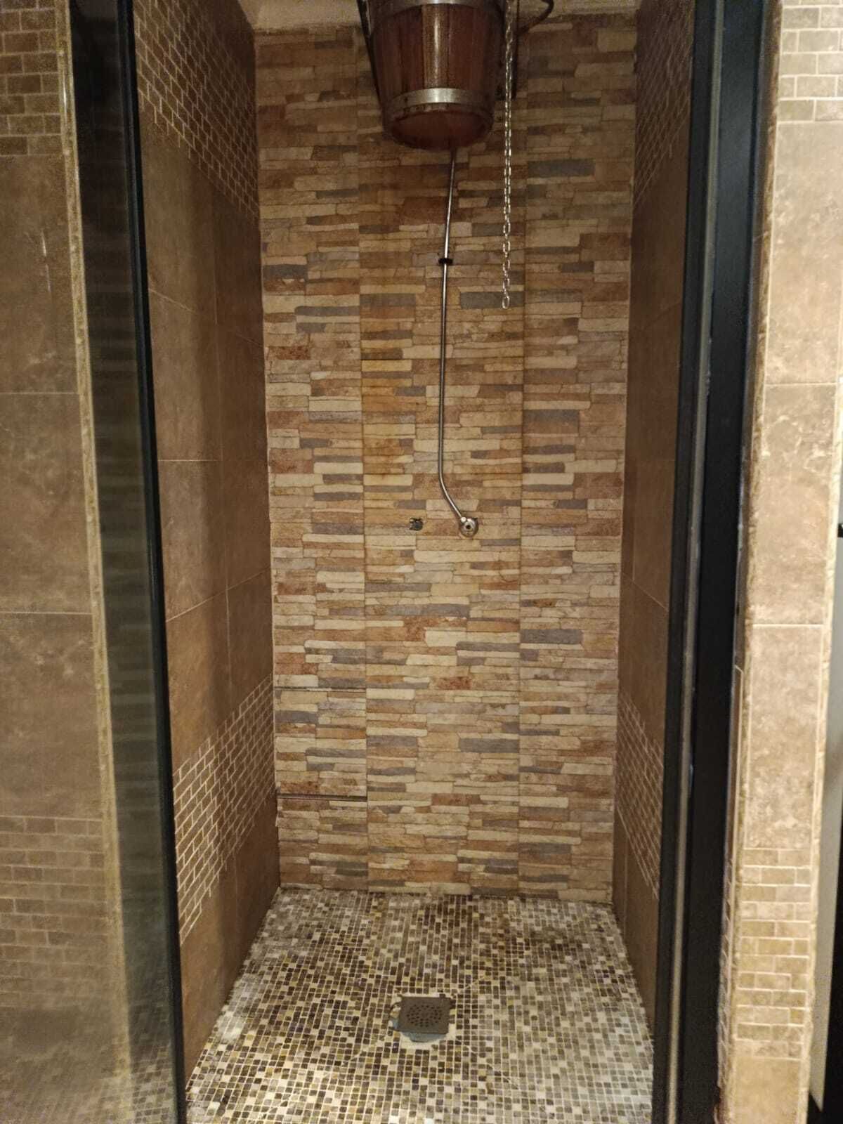 A shower with a tiled wall and floor, a metal showerhead, and a drain.