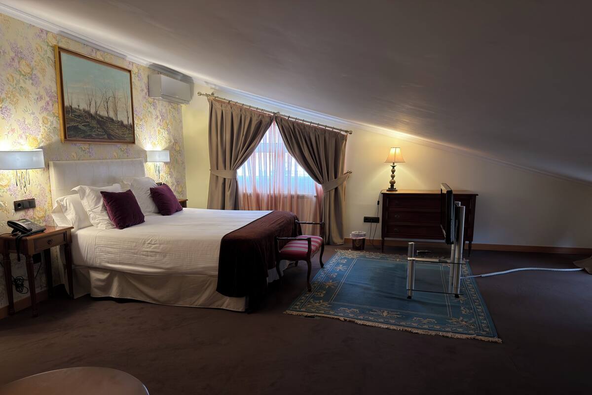 A bedroom with a bed, bedside table, lamp, chair, dresser, and a window with curtains.