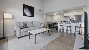 A modern living room with a sofa, coffee table, and a dining area with bar stools. - Meticulously Kept Downtown Mesa 1-Bedroom Oasis (Mesa)