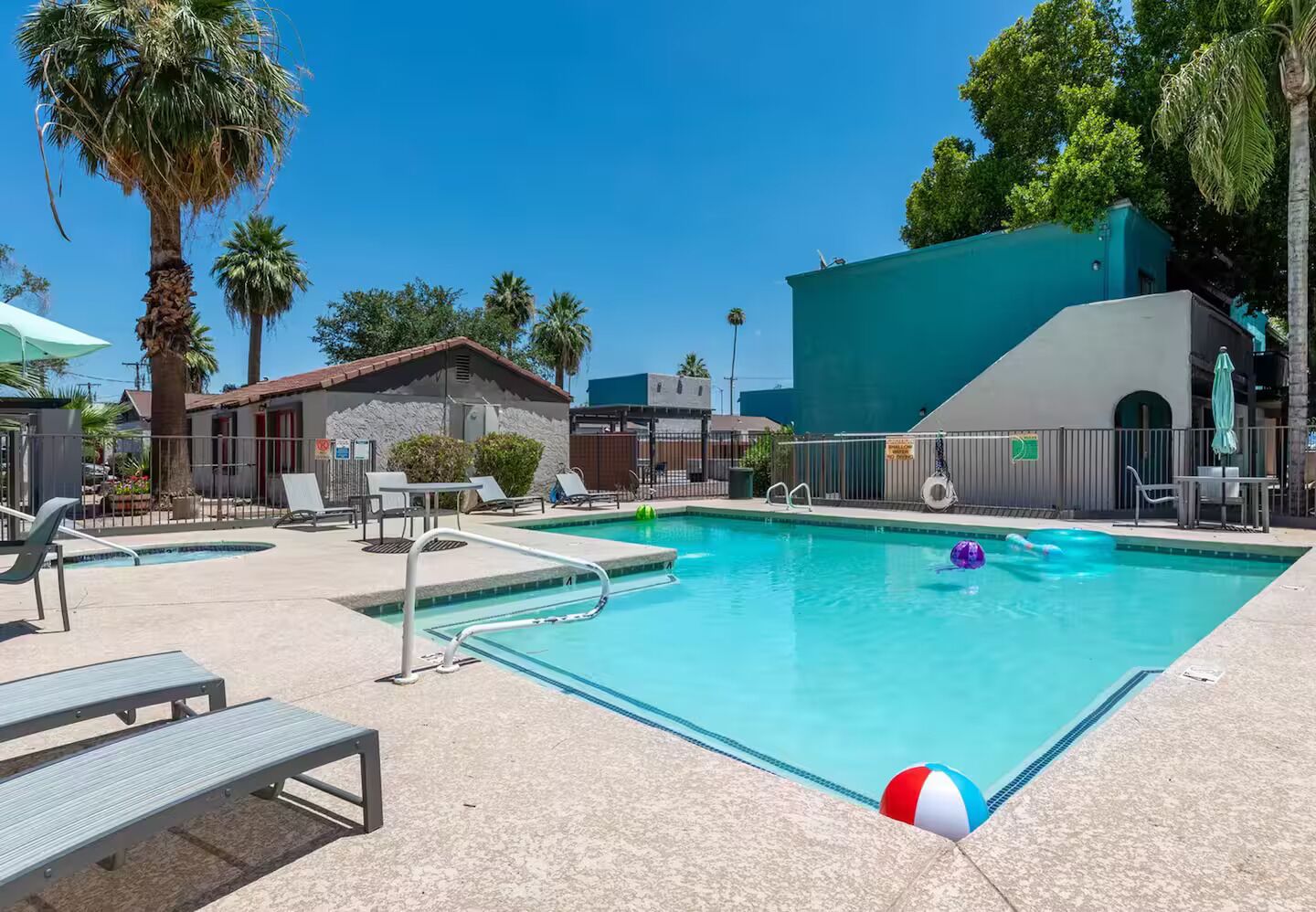 A rectangular swimming pool with a lifeguard chair, lounge chairs, and a beach ball.