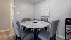 A round dining table with four grey chairs, a small potted plant, and a modern abstract painting on the wall. - Meticulously Kept Downtown Mesa 1-Bedroom Oasis (Mesa)