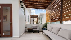 Un balcone con un divano, un tavolino e una sedia, sormontato da una pergola in legno.