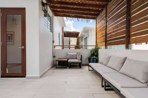 Ein Balkon mit einer Couch, einem kleinen Tisch und einem Stuhl, überdacht von einer Hollaube.
