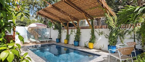 Una piscina con una pérgola de madera, sillas de descanso y plantas en macetas.