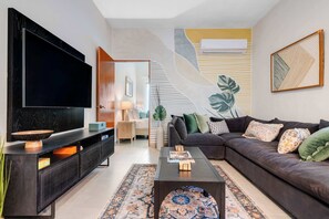 Ein modernes Wohnzimmer mit Flachbildfernseher, dunkelbrauner Ledersofa, gemustertem Teppich und schlichtem Wanddesign.