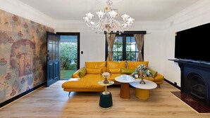 A living room with a sofa, a chandelier, a television, and a fireplace. - Luxury Glam Pool Retreat Near Glenelg Beach-sleeps 10 (Dover Gardens)