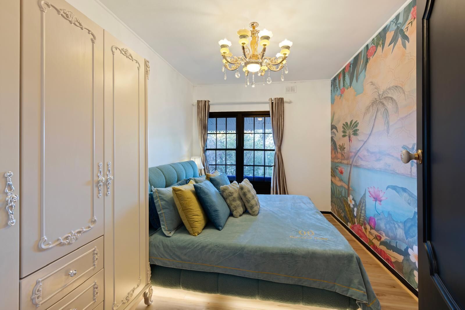 Ein Schlafzimmer mit einem Bett, einer Pendelleuchte, einem Kleiderschrank und einem Wandgemälde.