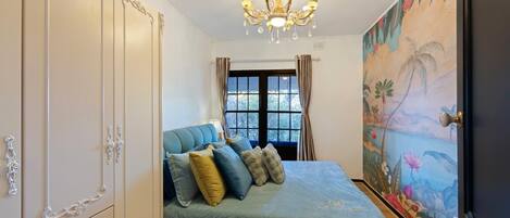 Ein Schlafzimmer mit einem Bett, einer Pendelleuchte, einem Kleiderschrank und einem Wandgemälde.