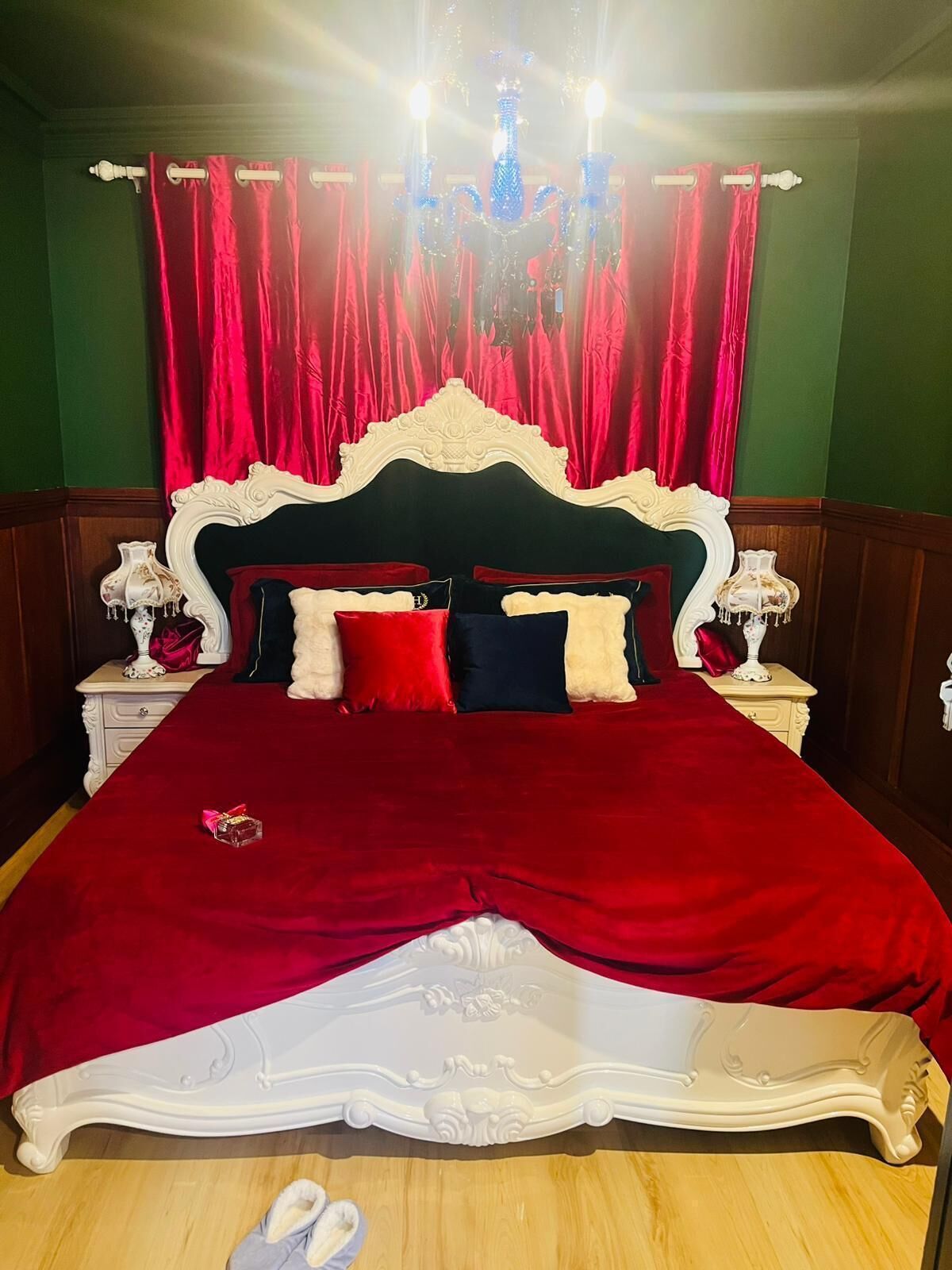 A bed with a white headboard, red and white bedding, and a chandelier.