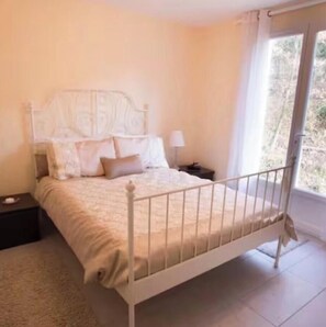 Une chambre à coucher avec un lit, une table de chevet, une lampe et une fenêtre.