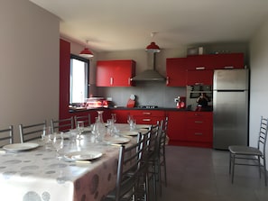 Een moderne keuken met rode kastjes, een roestvrijstalen koelkast, en een eetgedeelte met een tafel voor vier personen.