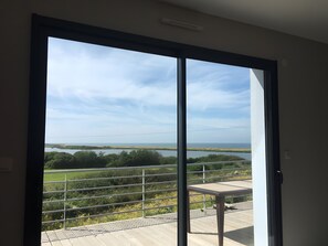Ein Zimmer mit einer großen Schiebetür, die auf einen Balkon mit Blick auf einen See und die Ferne führt.
