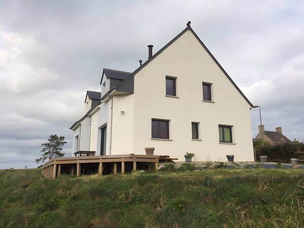 Une maison à deux étages, dotée d’un toit plat, de nombreuses fenêtres et d’une terrasse en bois.