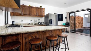 Eine moderne Küche mit Holzausstattung, einer großen Kochinsel mit Sitzgelegenheiten, Edelstahlgeräten und einer Glastür zum Patio.