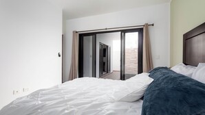 Ein Schlafzimmer mit Bett, Blick durch eine Schiebetür und Deckenleuchte.