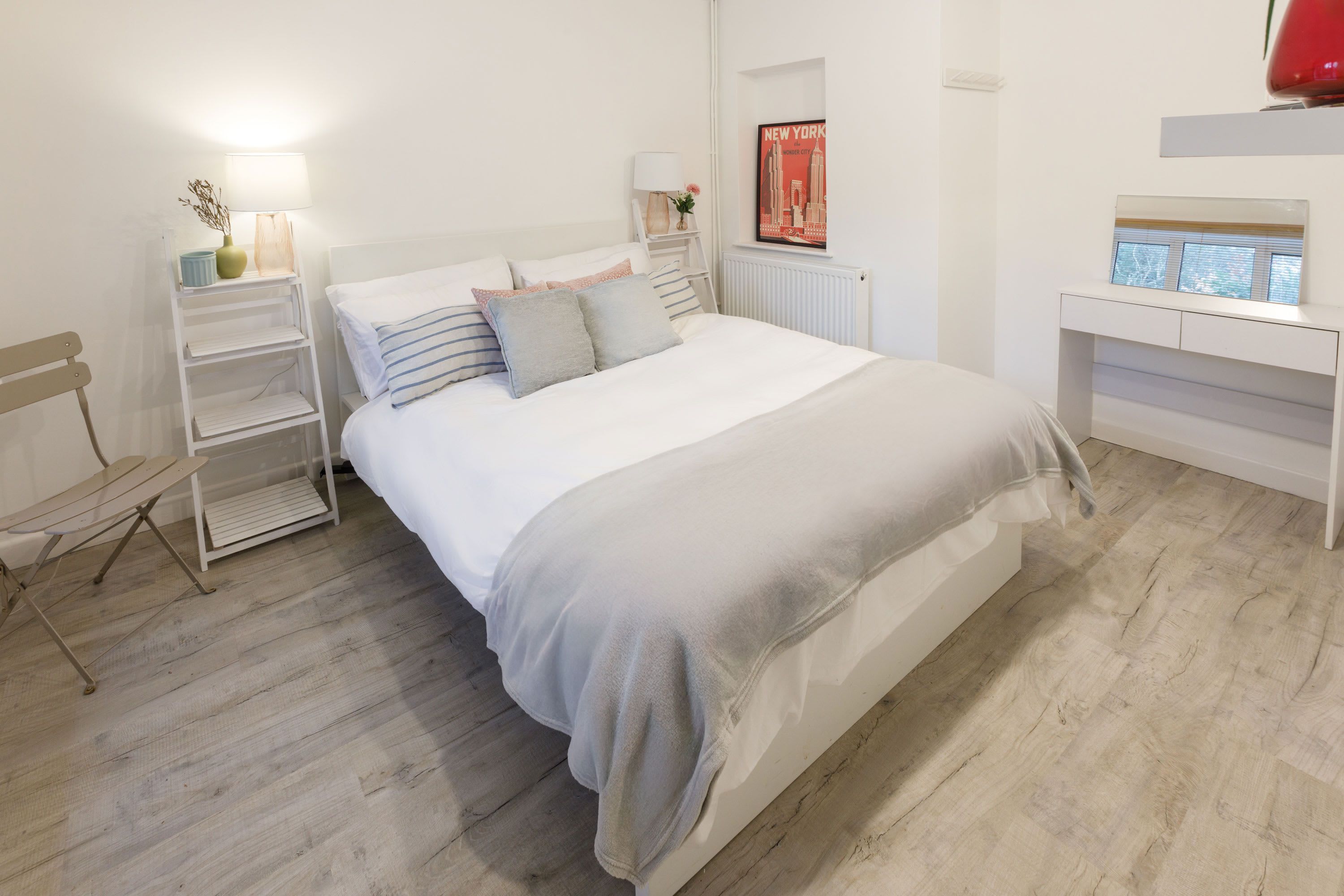 Un dormitorio ordenado con cama, mesitas de noche, una silla y un radiador.