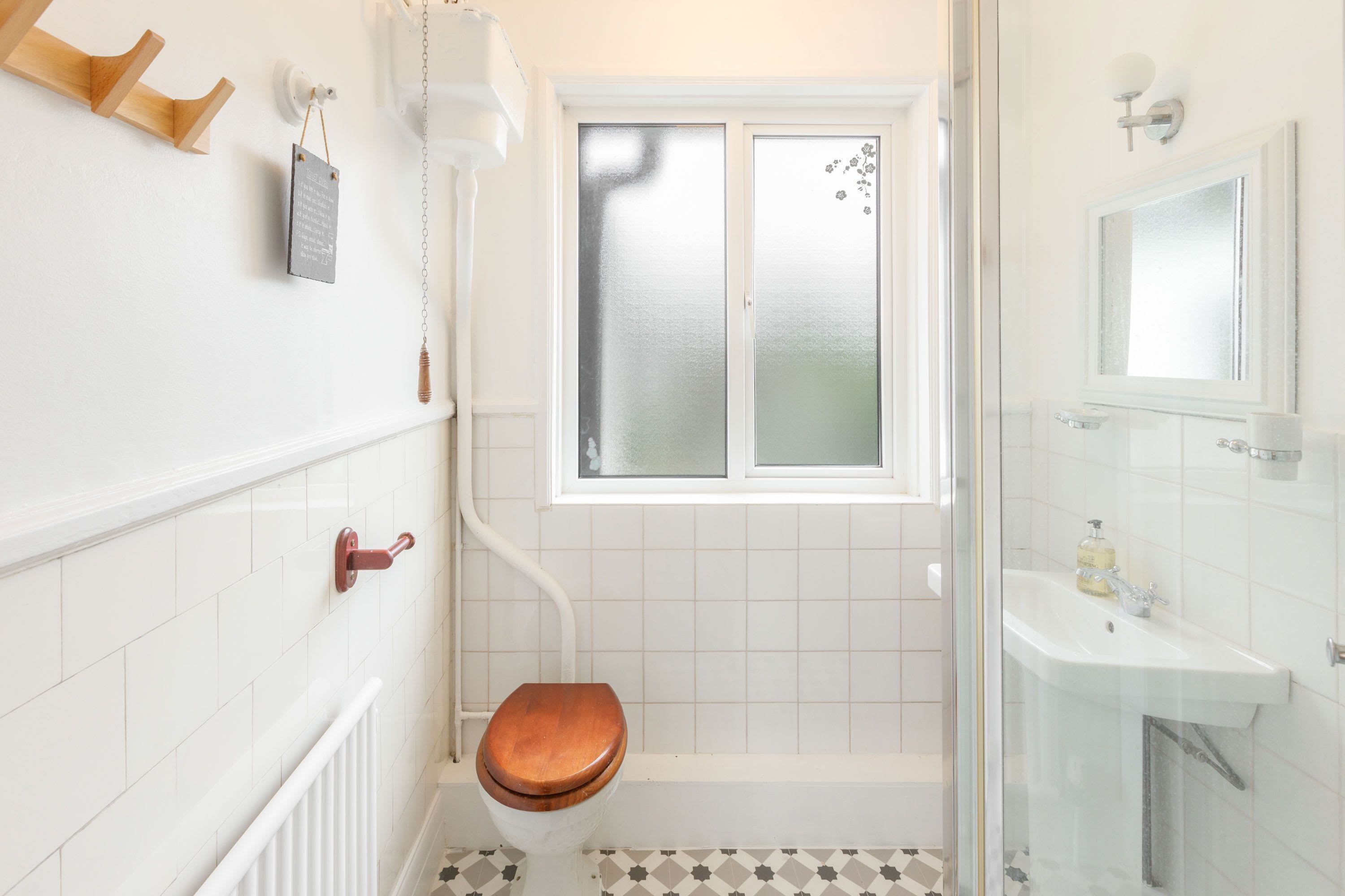 A bathroom with a wooden toilet, a window, a sink, and a mirror.