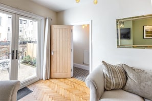 Um quarto com piso em padrão herringbone, porta de vidro deslizante para área externa, sofá com almofadas e espelho emoldurado na parede.