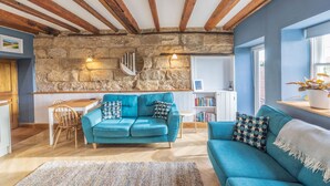 Un salon chaleureux avec un mur en pierre, des poutres apparentes, un canapé bleu et un coin repas.