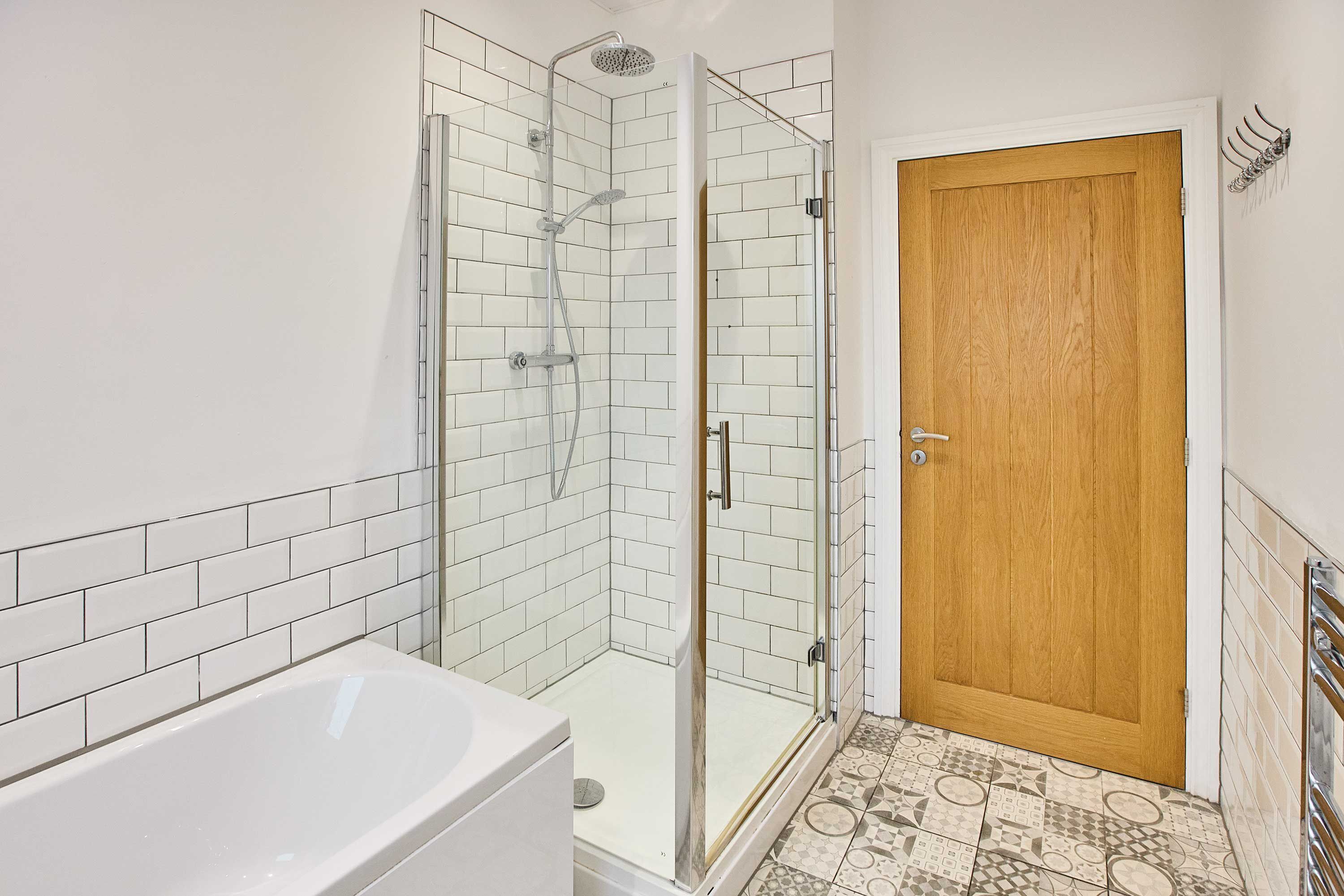 A bathroom with a glass shower enclosure, a white bathtub, and a wooden door.