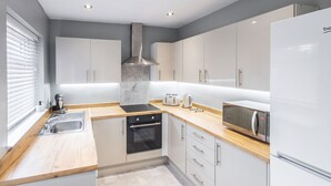 A modern kitchen with white cabinets, a stainless steel range hood, a built-in oven, a microwave, and a sink. - Host Stay Elmville (Scarborough)