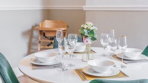 A round dining table set with white plates, bowls, and wine glasses, a gold napkin, and a vase with flowers. - Host Stay Elmville (Scarborough)