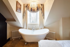 A bathroom with a freestanding bathtub, a window with curtains, a radiator, and a chandelier. - Host Stay Osbourne Apartment (Newcastle-upon-Tyne)