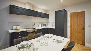 Een moderne keuken met donkere kastjes, een wit aanrecht en een eethoek voor vier personen.