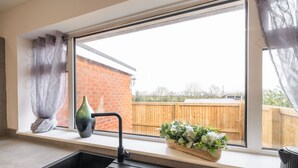 A kitchen with a black sink, a window with a view of a brick building and a wooden fence, and a potted plant on the windowsill. - Host Stay Hawthorn Bank (Leeds)