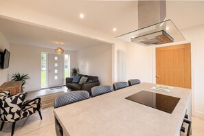 A modern kitchen with a central island, a dining area with chairs, a sofa, and a TV mounted on the wall. - Host Stay Hawthorn Bank (Leeds)