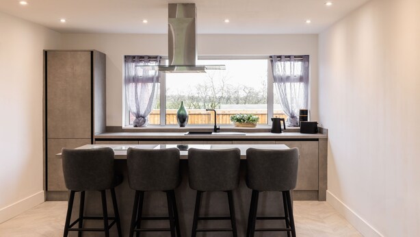 A modern kitchen with a large window, bar stools, and a stainless steel range hood. - Host Stay Hawthorn Bank (Leeds)