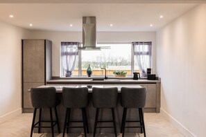 A modern kitchen with a large window, bar stools, and a stainless steel range hood. - Host Stay Hawthorn Bank (Leeds)