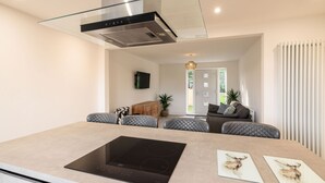 A modern kitchen with a glass cooktop, a built-in range hood, and a seating area with cushioned chairs. - Host Stay Hawthorn Bank (Leeds)