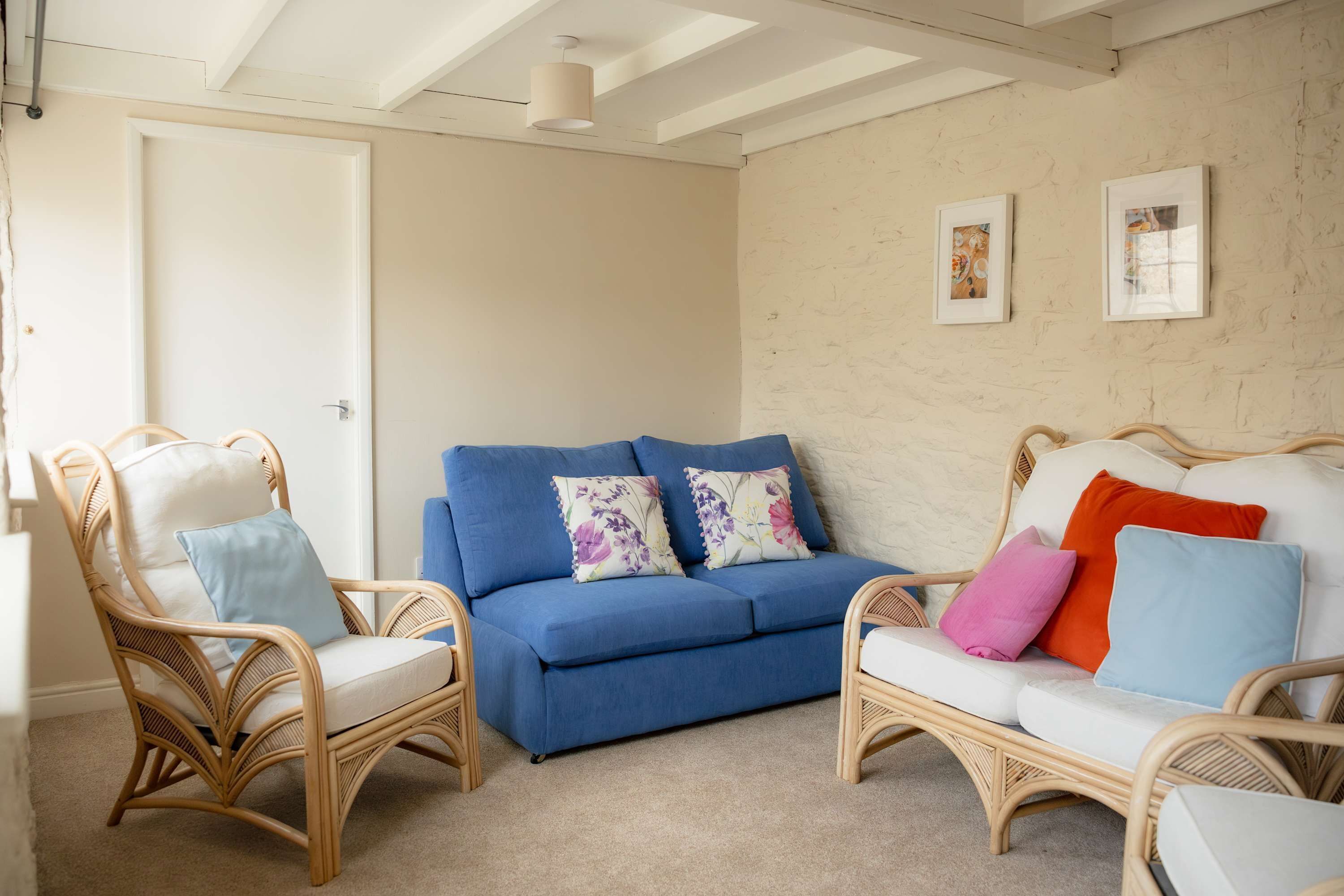 Una habitació amb un sofà blau, cadires de vimet i un sofà blanc amb coixins de colors.