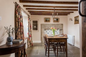 A dining area with a wooden table, chairs, a vase of flowers, and a tiled backsplash. - Host Stay Corner House (York)