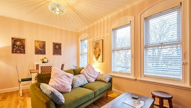 A cozy room with a green sofa, a wooden table, and a chair. There are three wall-mounted artworks and a vase on a side table. - Host Stay Stay Salty (Saltburn-by-the-Sea)