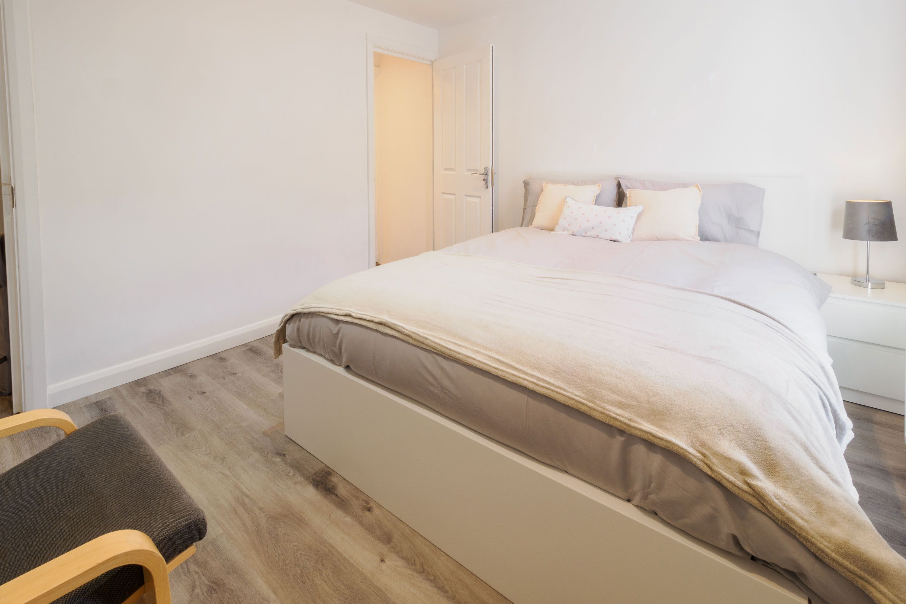 A bedroom with a bed, bedside table, lamp, and a chair.