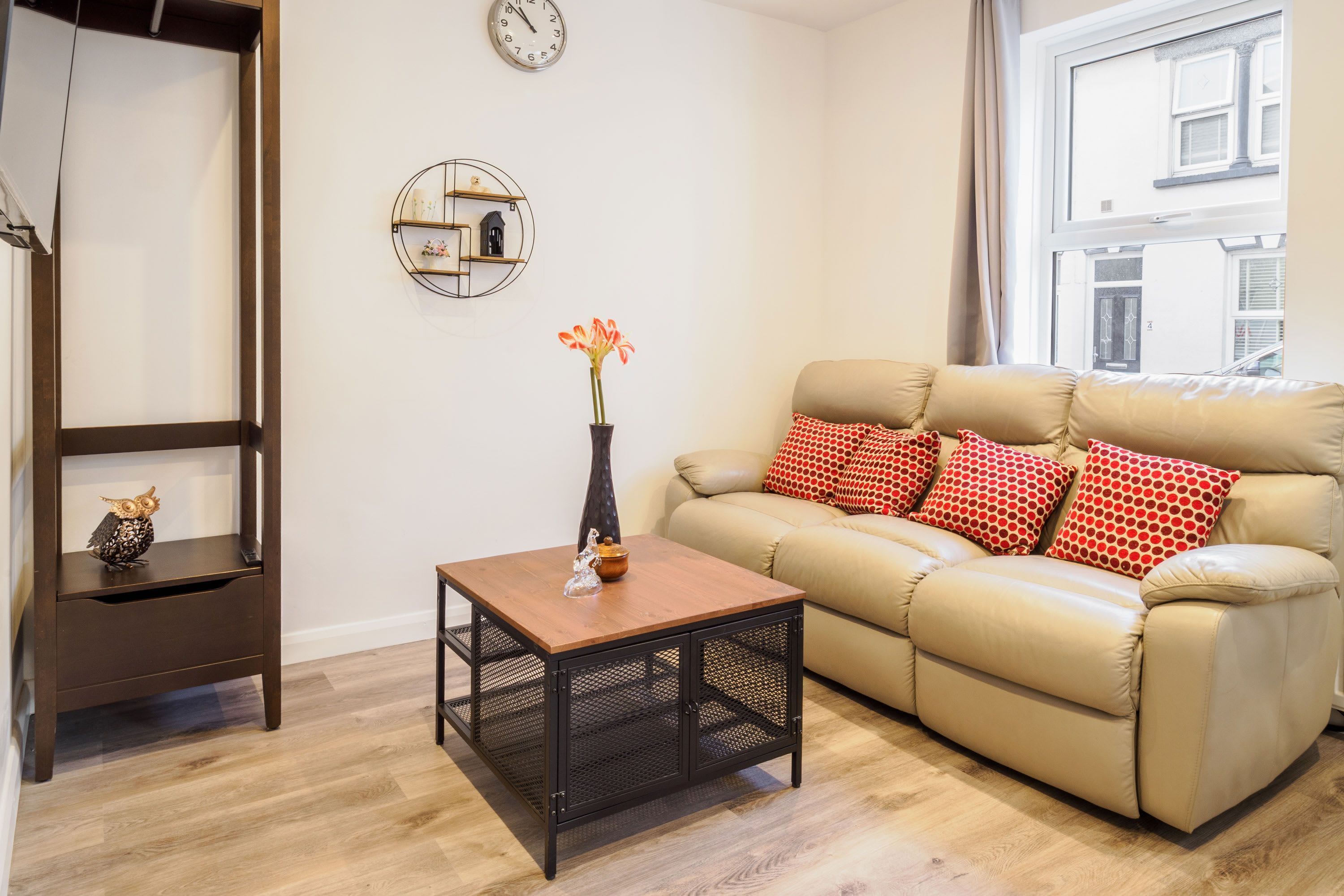Un salon comprenant un canapé, une table basse, une table d’appoint, une horloge murale et une étagère décorative.