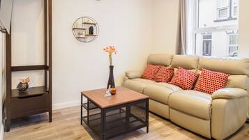 A living room with a sofa, a coffee table, a side table, a wall clock, and a decorative shelf.