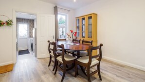 A dining area with a round table, six chairs, a wooden cabinet, and a view of a laundry room through an open door. - Host Stay Roach Street (Rochester)