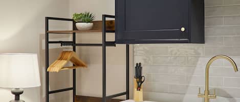A kitchen with a white countertop, a gold faucet, and a black metal shelf with a plant.