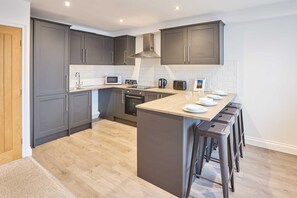 A modern kitchen with grey cabinets, a central island with stools, a microwave, and a stove. - Host Stay Sandcastle Apartment (Blackpool)