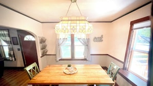 A dining room with a wooden table, chairs, a hanging light fixture, and a window with curtains.