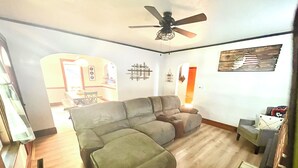 A living room with a sectional sofa, a ceiling fan, and a dining area in the background.