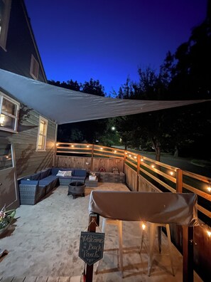 A covered outdoor seating area with a sofa, a table, and a sign that reads 'Welcome to the Back Porch.' - Clearwater Cottage – Cozy Historic Home Near the River (Orofino)