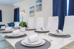 Ein Essbereich mit einem langen Tisch, gedeckt für eine Mahlzeit, einschließlich Tellern, Tassen und einem Blumentopf.
