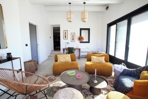 A modern living room with a sofa set, a wicker chair, a coffee table, and a large window. - Maison typique à Gordes entre pierre, lavande et soleil. Service de conciergerie (Gordes)