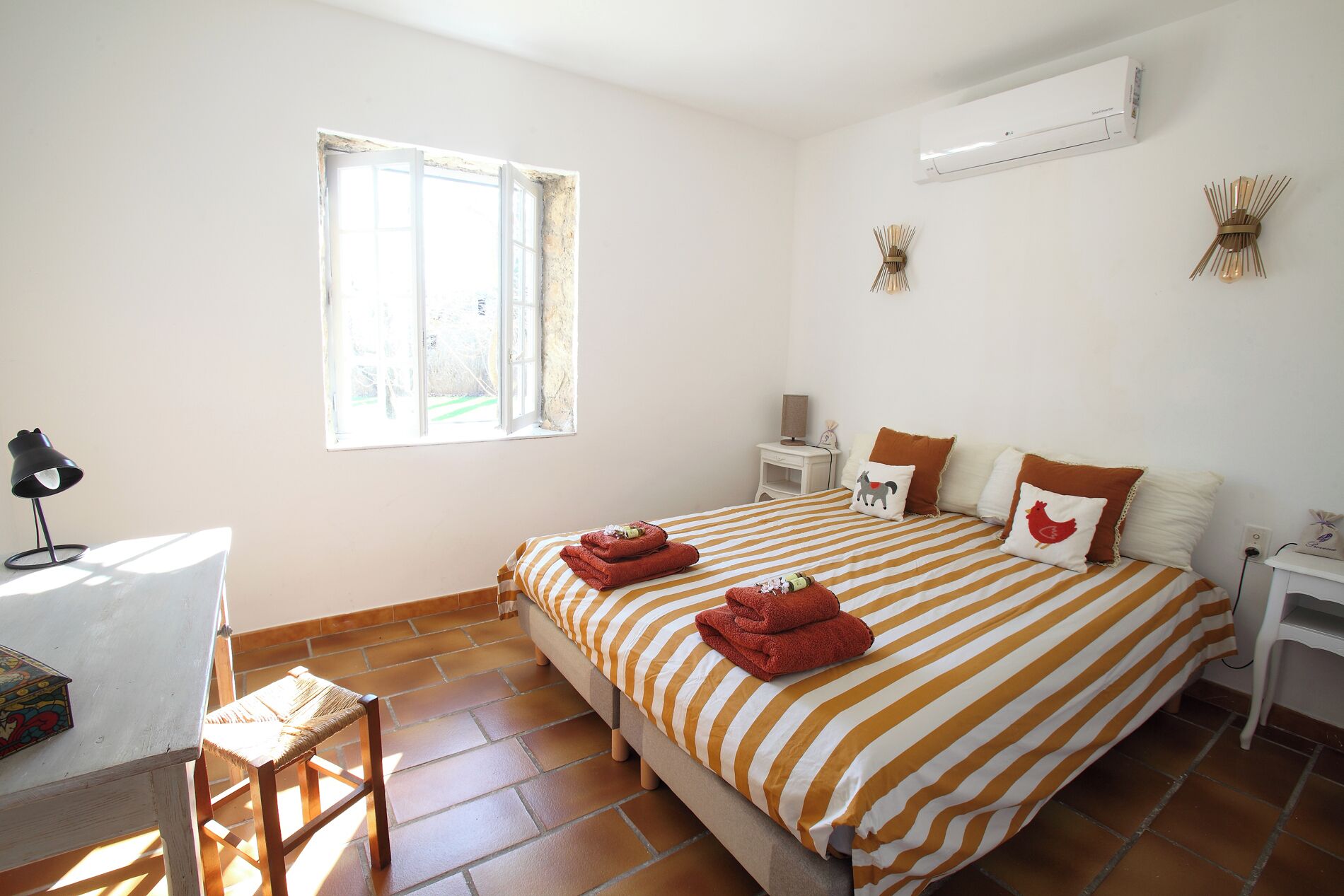 A bedroom with a bed, a desk, a chair, a window, and an air conditioning unit.